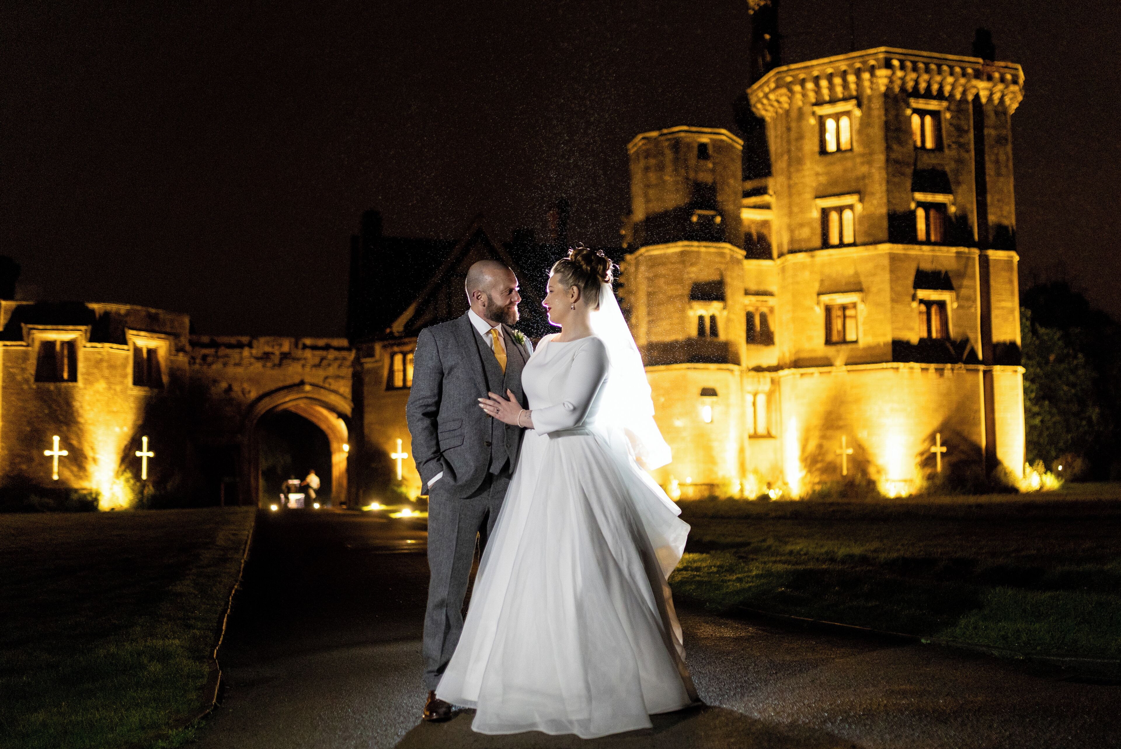 A couple in front of a castle-like building at night.