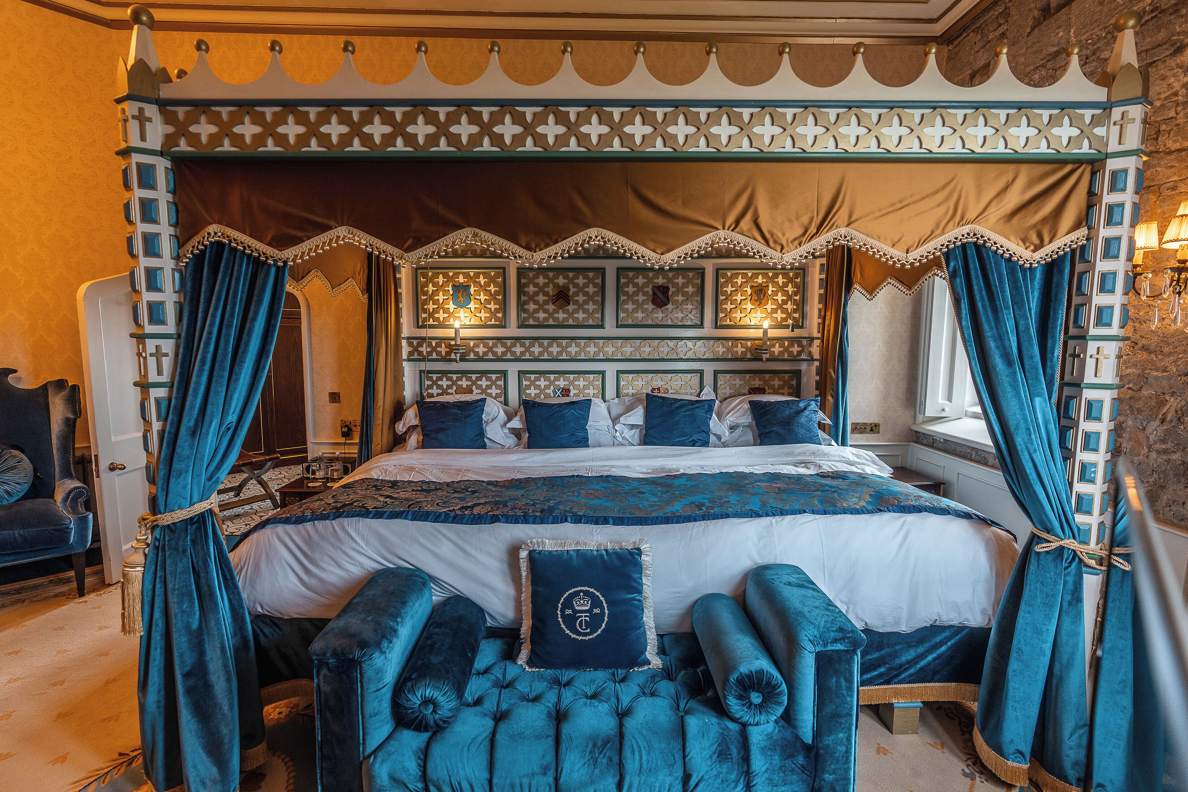 Una cama con dosel y cuatro columnas, con un cabecero decorativo tapizado en azul y cortinas a juego.