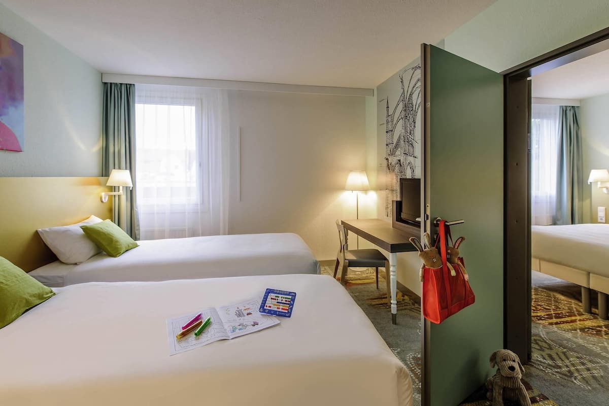 Habitación de hotel con dos camas, un escritorio, un televisor y una puerta con un bolso rojo colgado.