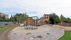 Un'area giochi con struttura da arrampicata e scivoli, circondata da una superficie pavimentata con rocce e un bordo in prato.
