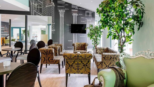 Un'area lounge moderna con poltrone a fantasia e un divano verde, una pianta grande e un televisore montato a parete.