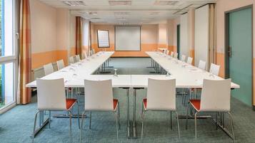 Un salón de conferencias con una larga mesa, sillas blancas y una pantalla para proyector.