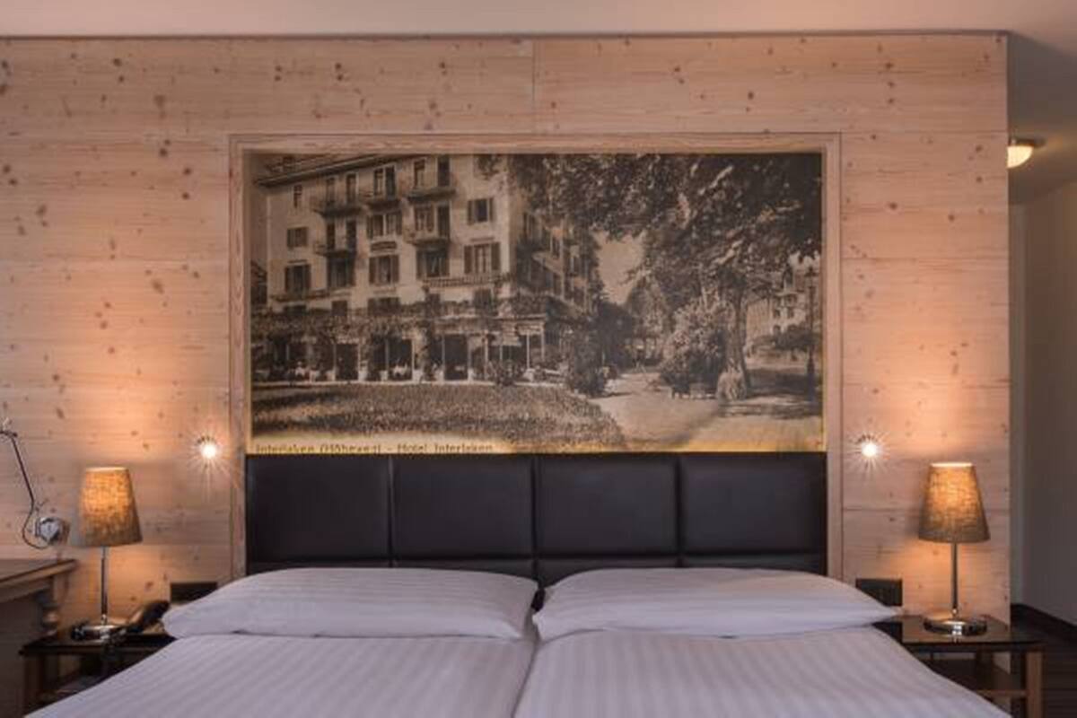 A hotel room with a large bed, two bedside lamps, a wooden headboard, and a large framed picture on the wall.