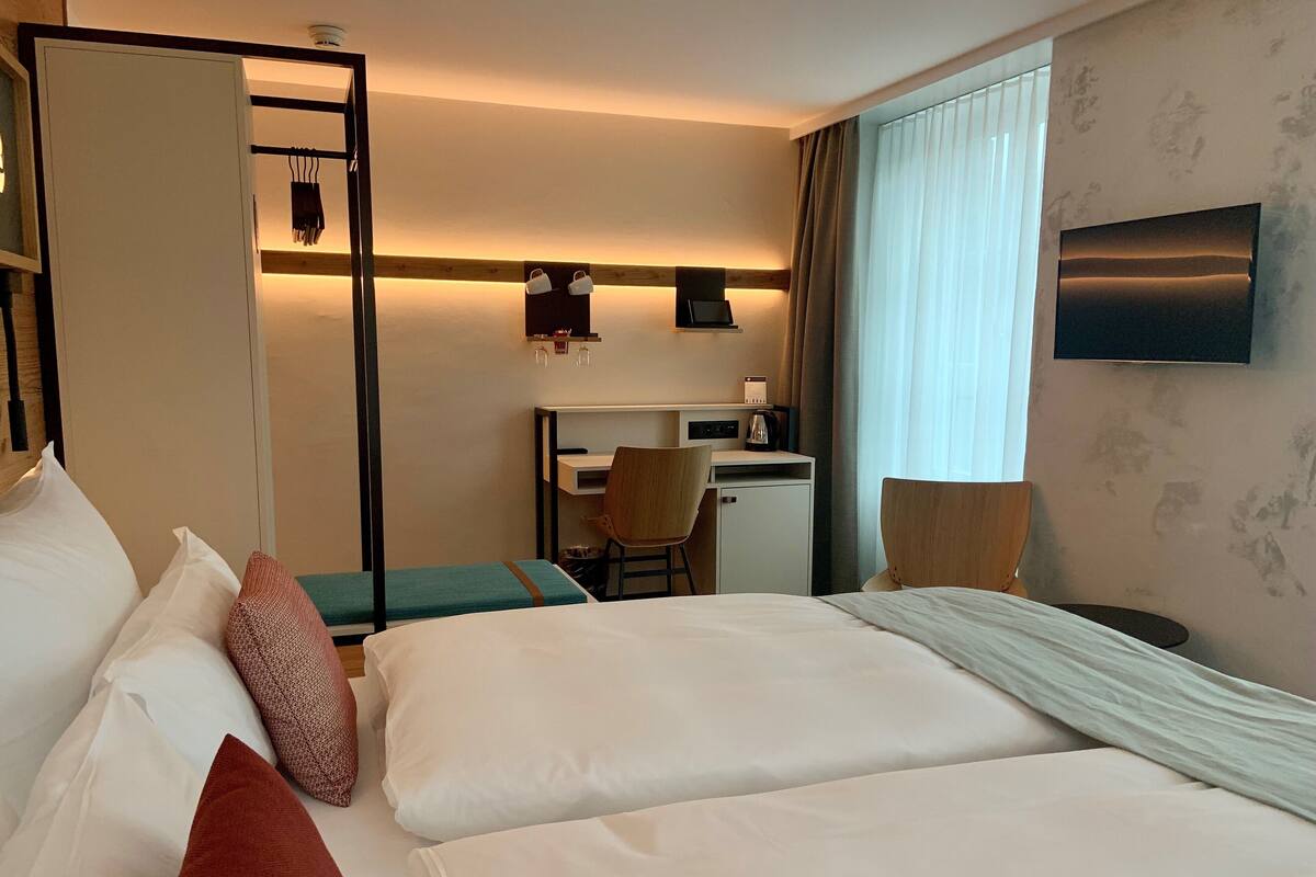 A hotel room with two beds, a desk, a chair, and a TV.