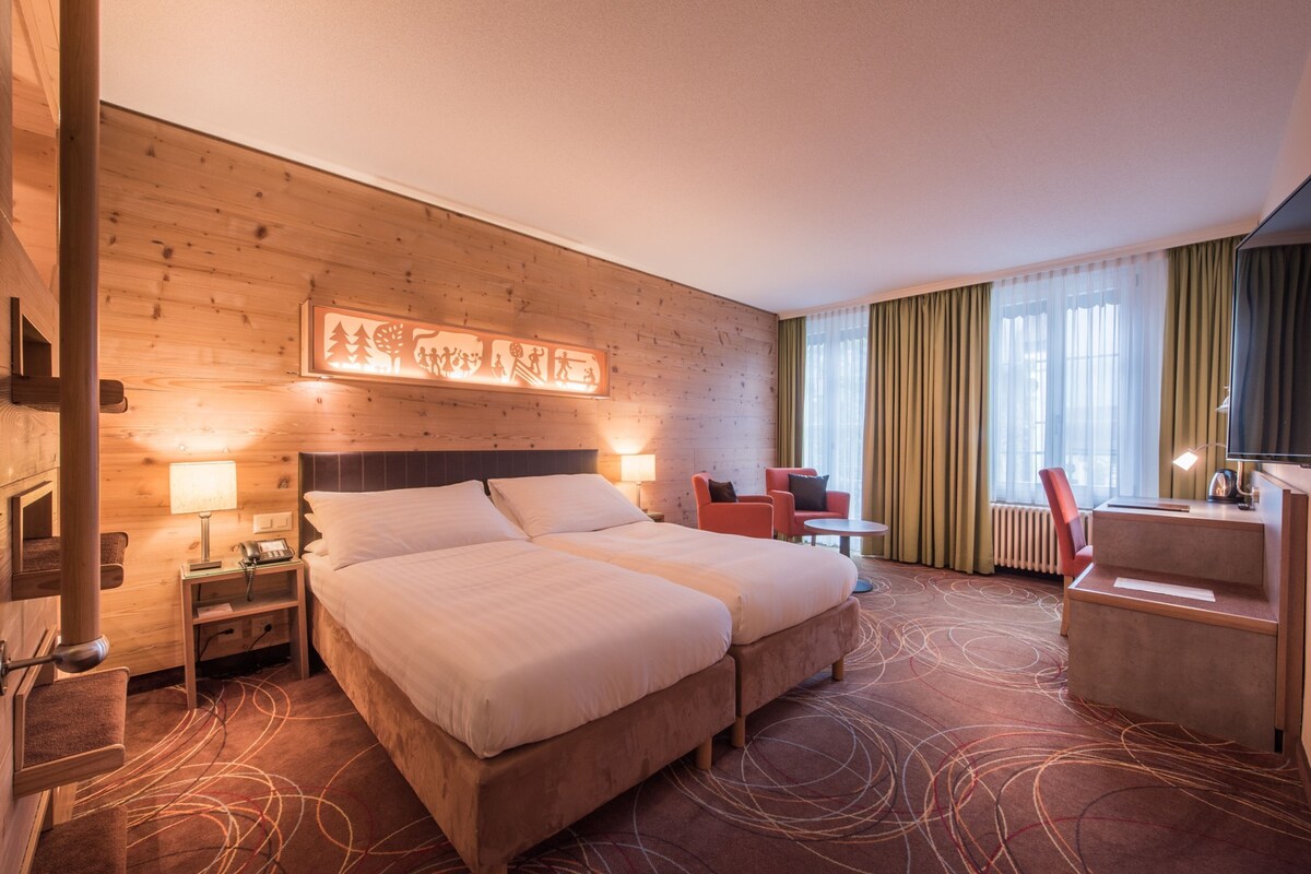 Habitación de hotel con una cama grande, un escritorio, una silla, una lámpara y una obra de arte colgada en la pared.