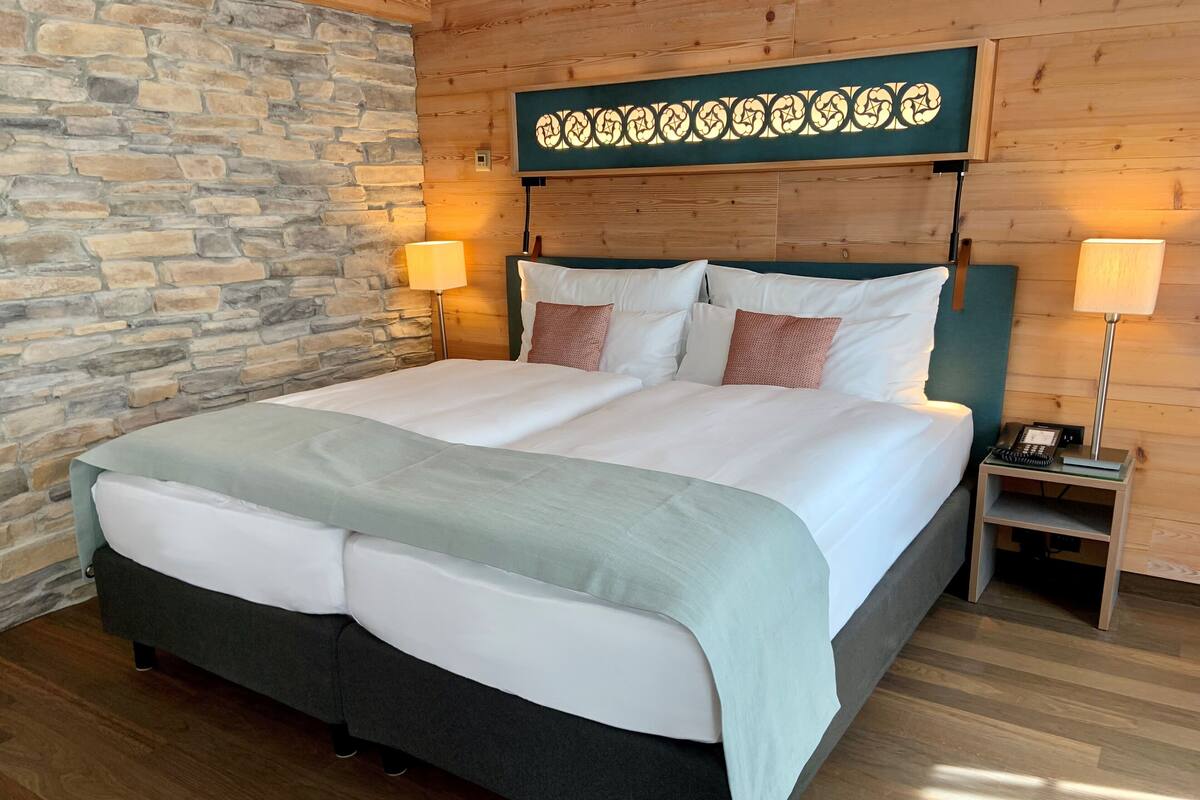 A double bed with a green headboard, two bedside tables with lamps, and a stone wall.