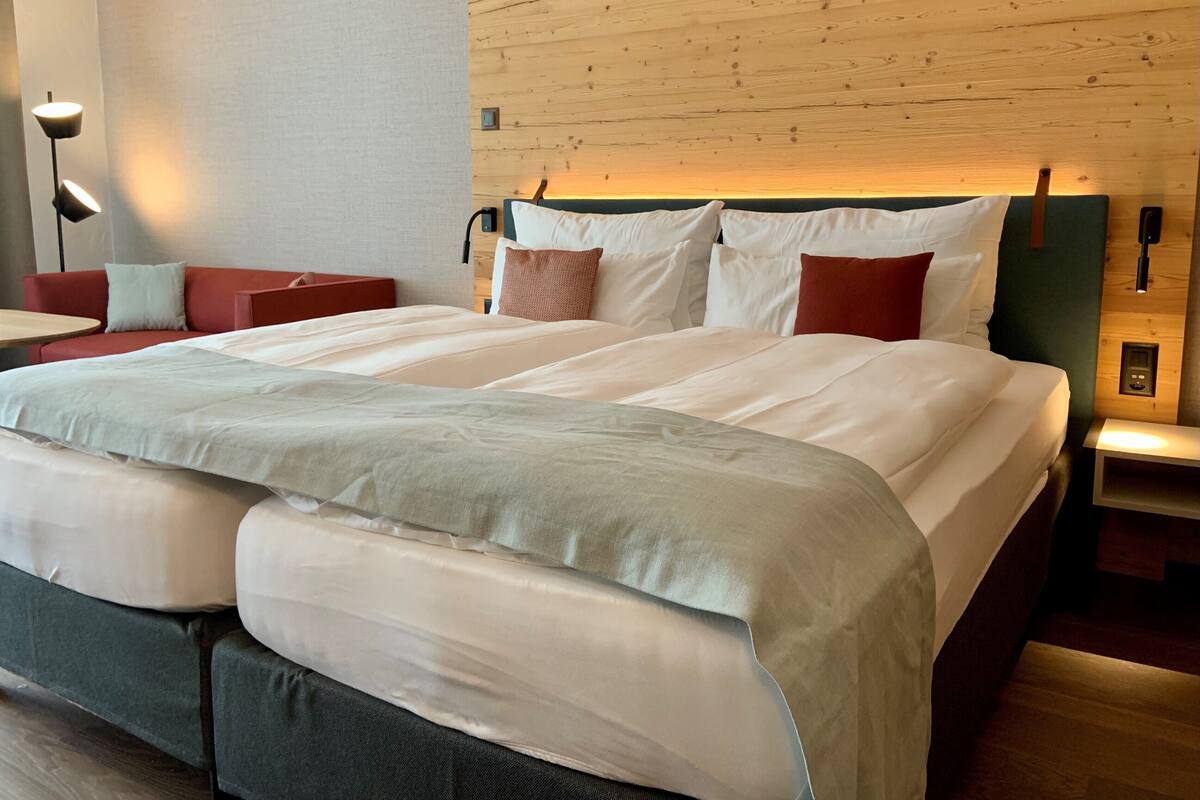 A modern hotel room with a large bed, a red sofa, a desk, and a wooden accent wall.