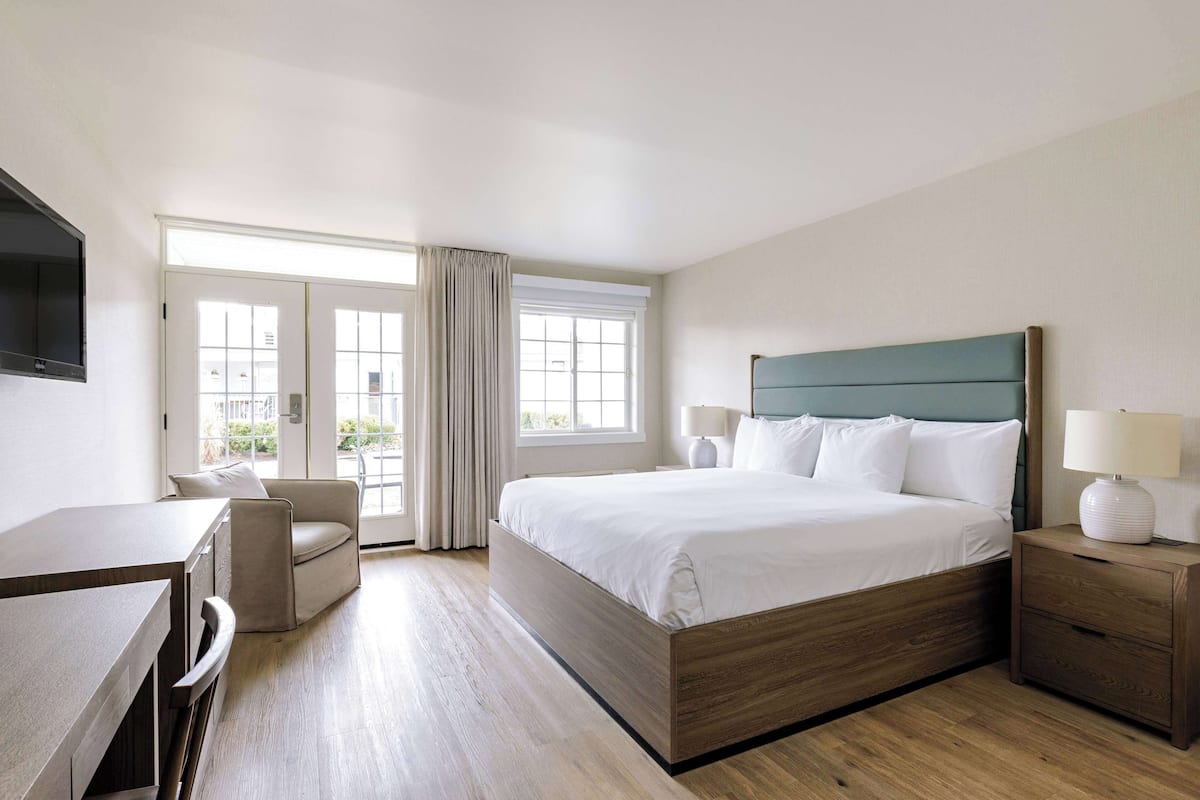 A hotel room with a bed, a desk, a chair, a nightstand, and a TV.