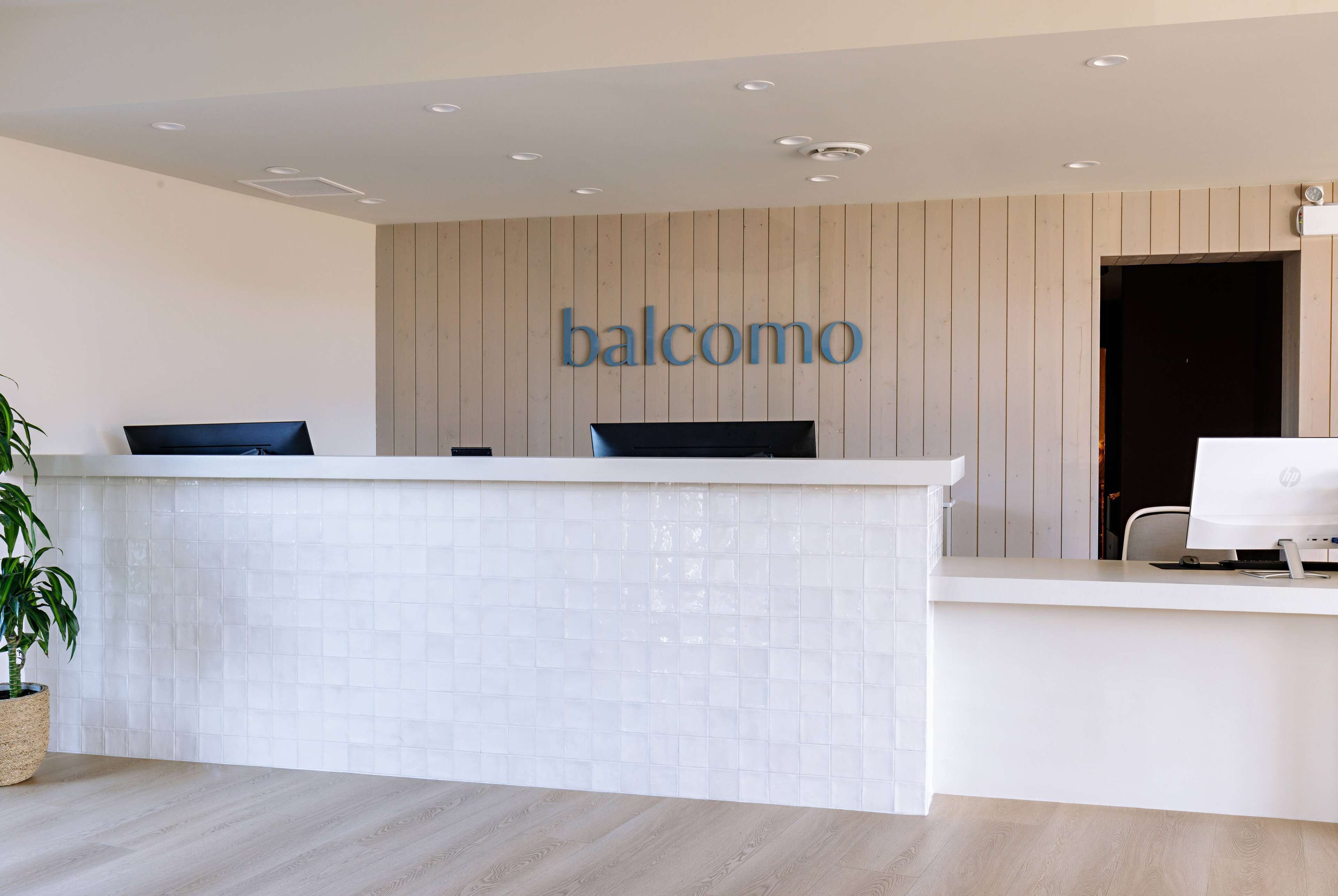 A reception desk with a 'balcomo' sign, a potted plant, and a computer monitor.
