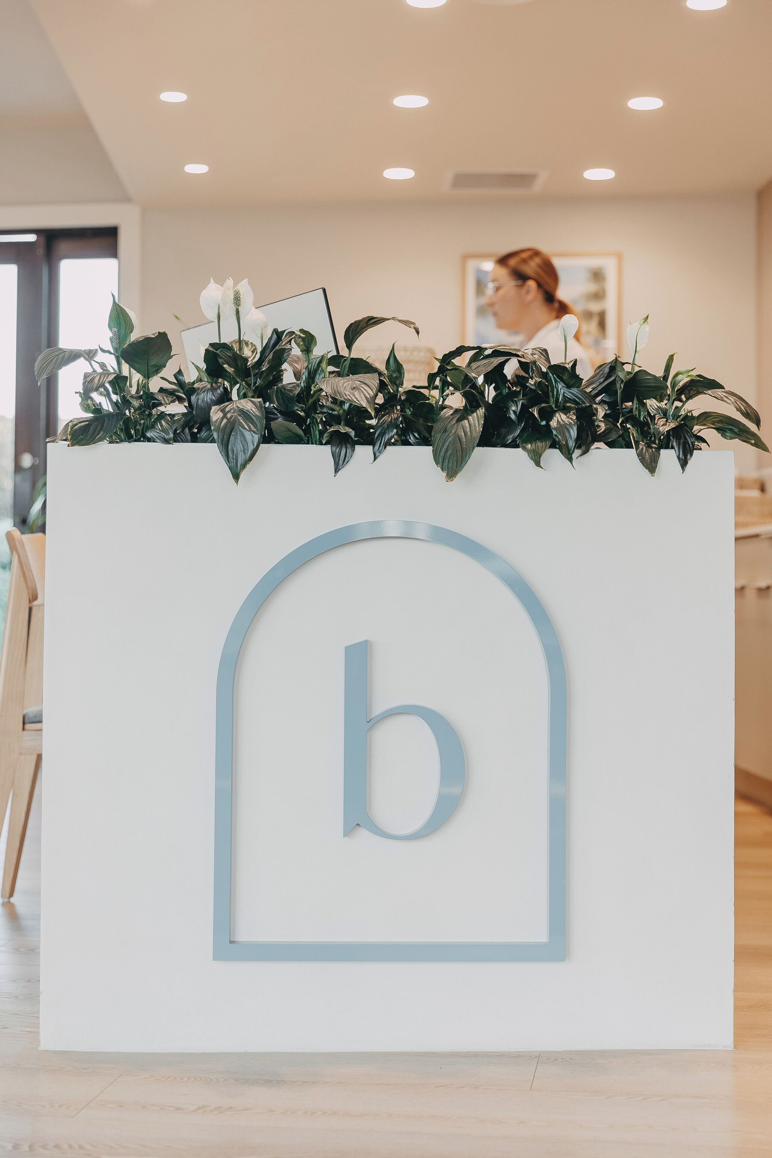 A reception desk with a logo, surrounded by potted plants.