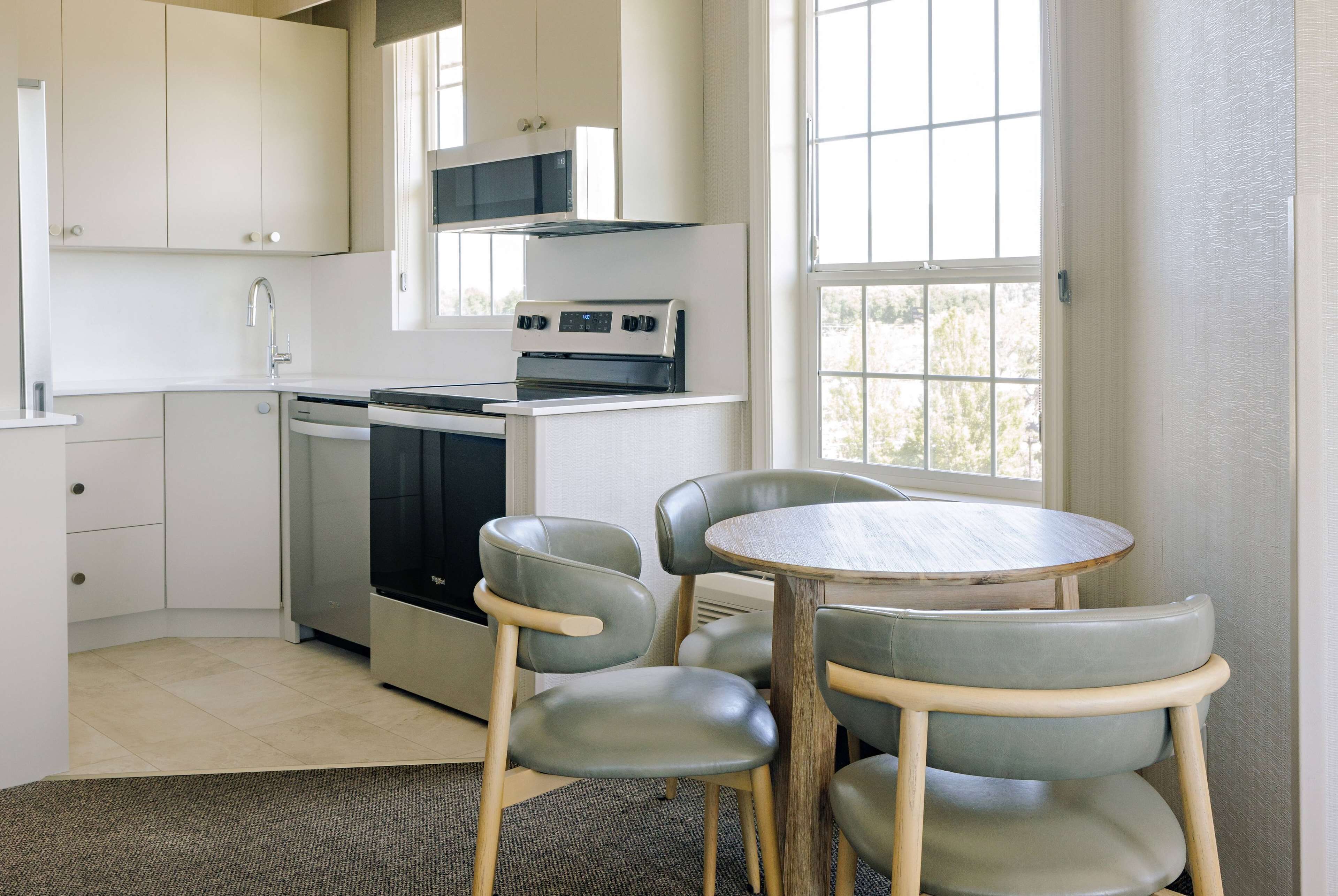Cocina compacta con armarios blancos, microondas y estufa. Zona de comedor con mesa redonda y cuatro sillas.