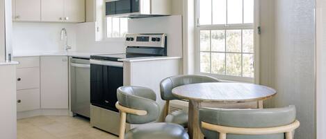 Cocina compacta con armarios blancos, microondas y estufa. Zona de comedor con mesa redonda y cuatro sillas.
