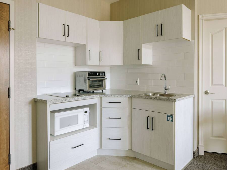 Een kleine keuken met witte keukenkastjes, een ingebouwde magnetron, een fornuis en een spoelbak.