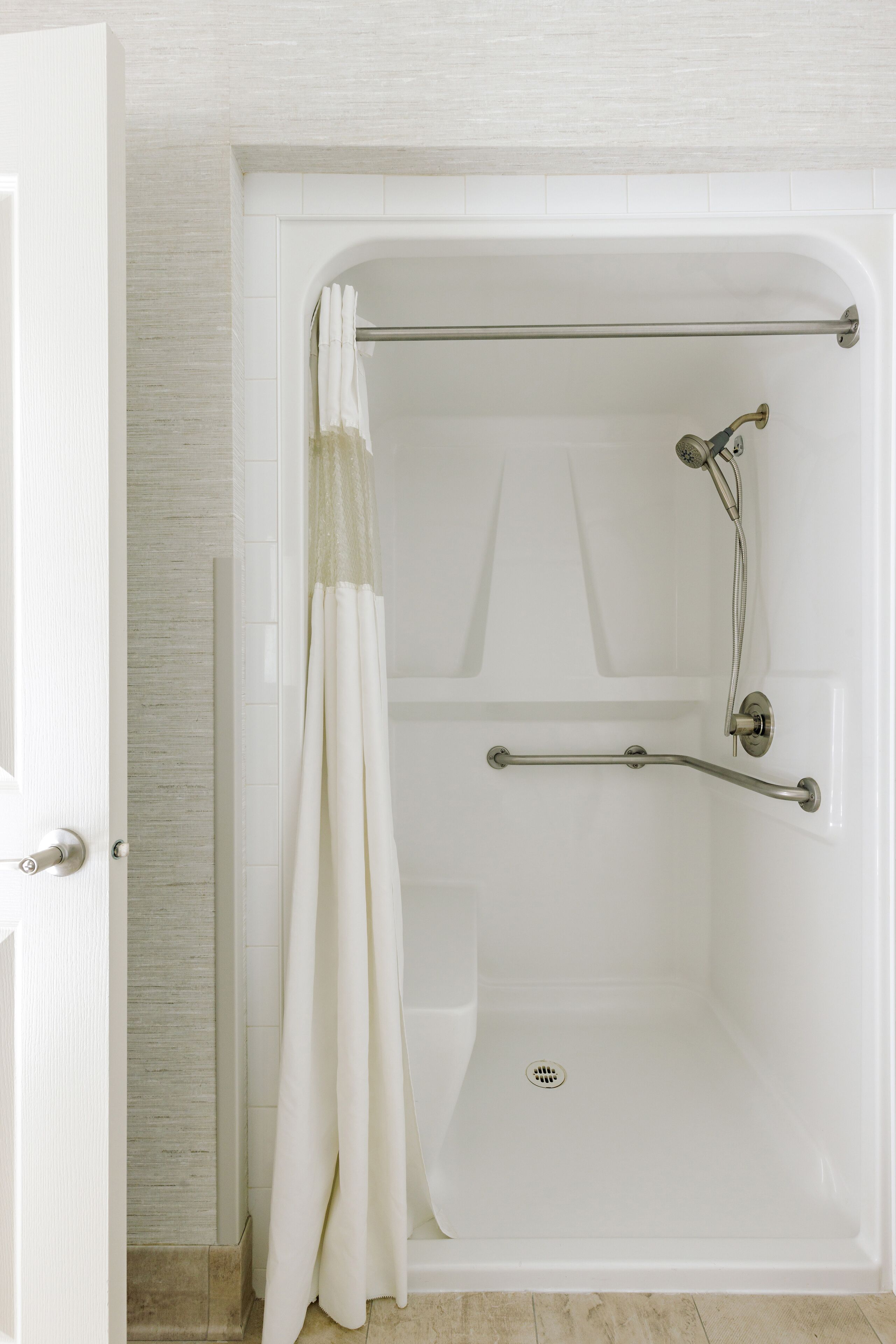 A walk-in shower with a grab bar, a showerhead, and a curtain.