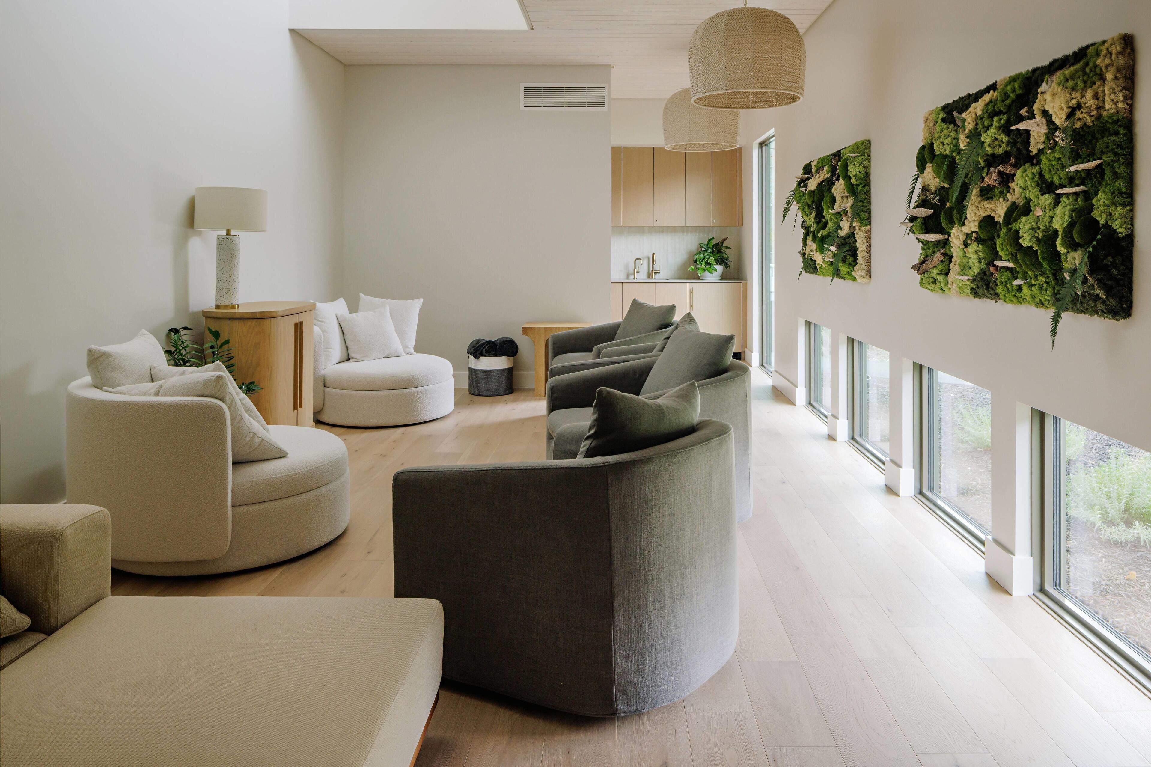 A modern living room with a sofa, armchairs, a lamp, and a wall-mounted plant.
