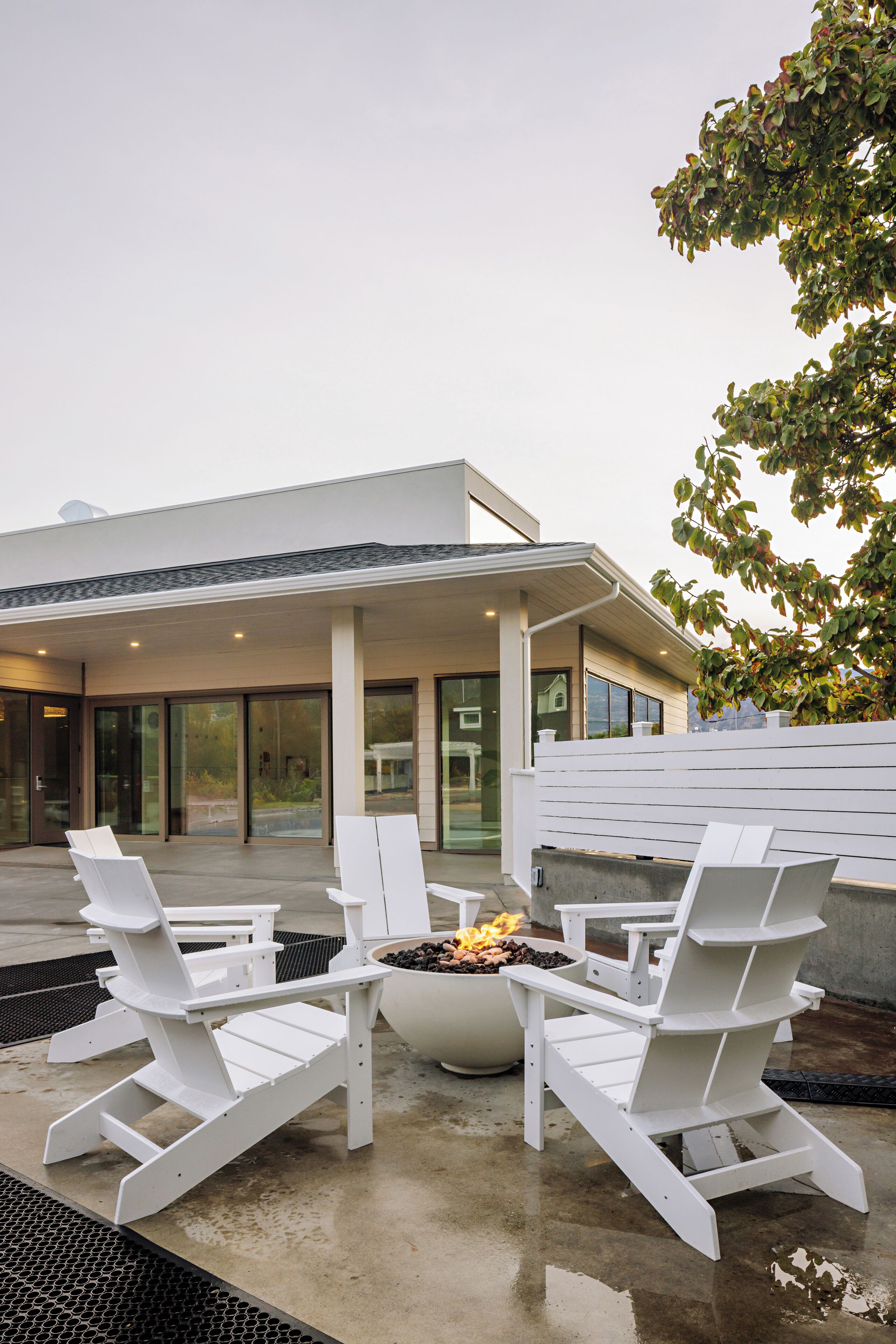 A modern outdoor seating area with Adirondack chairs and a fire pit.