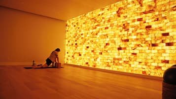 A person performing a yoga pose on a mat in a room with a wooden floor and a wall with a textured pattern.