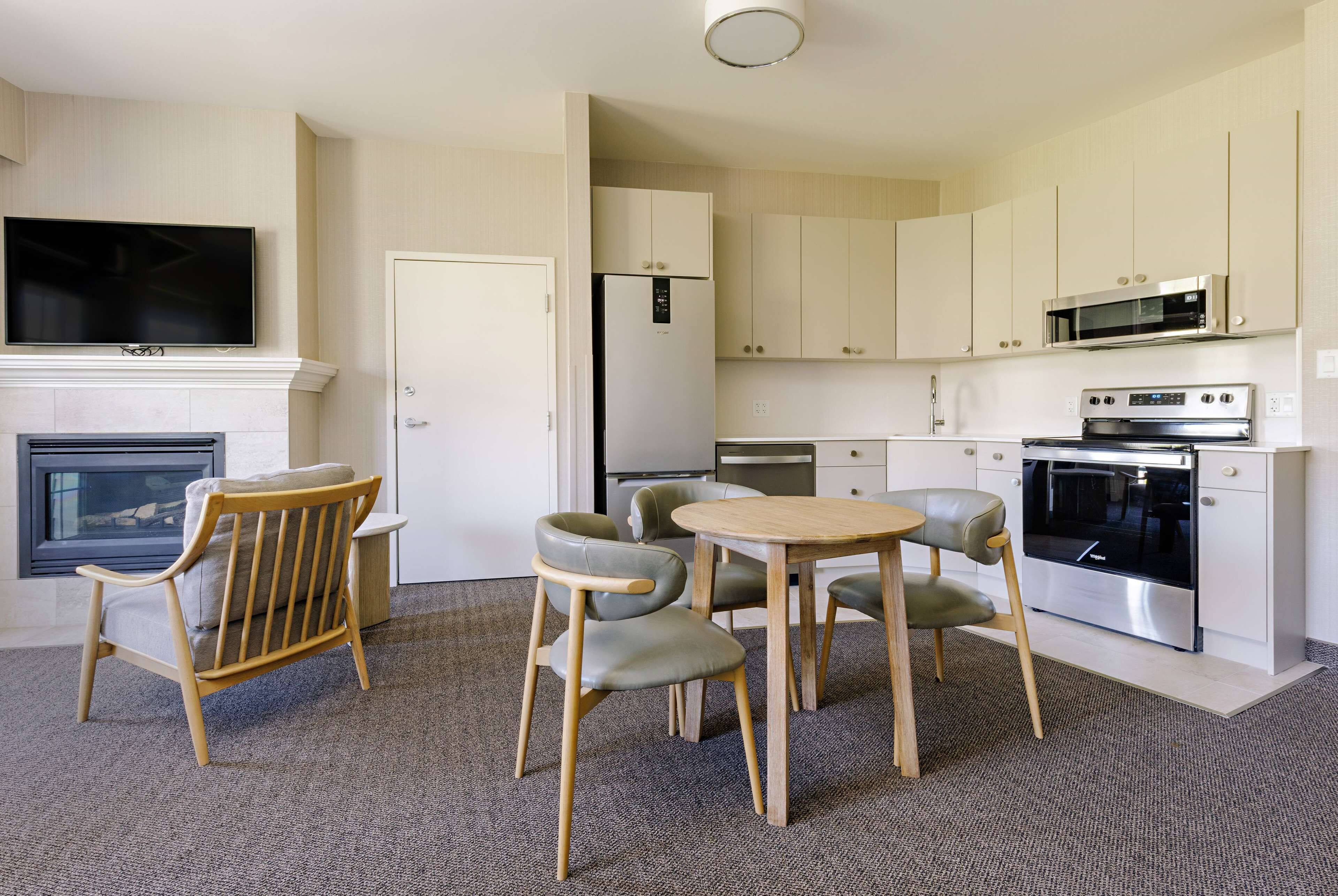 A modern kitchen with white cabinets, a built-in oven, and a microwave. There is a dining area with a wooden table and chairs.
