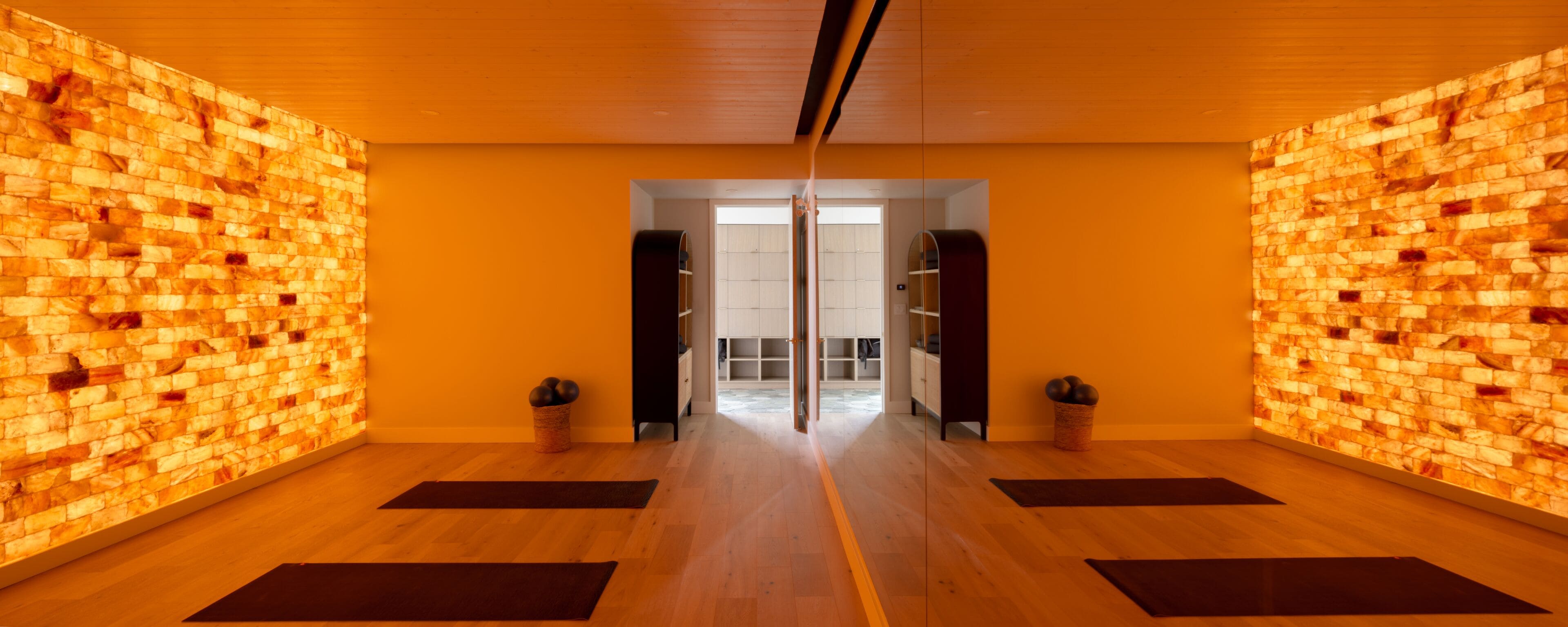 A room with wooden floors, a mirrored wall, and a door leading to a bathroom.