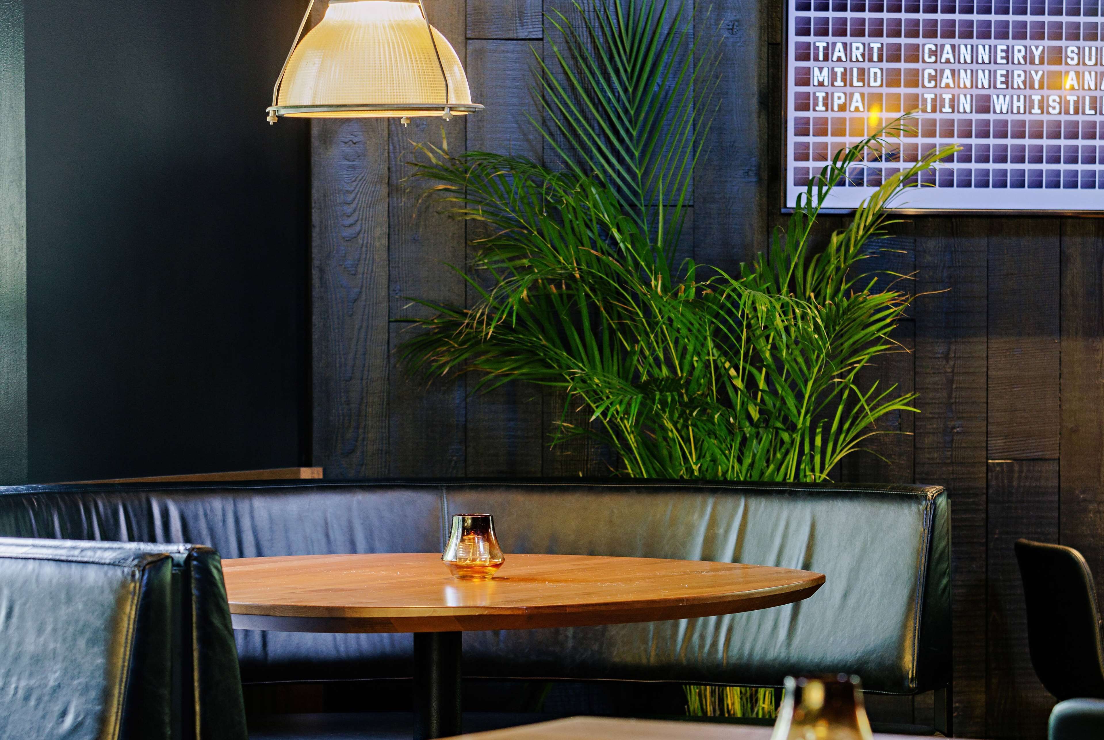 A cozy restaurant interior with a wooden table, leather booth seating, and a wall-mounted menu board.