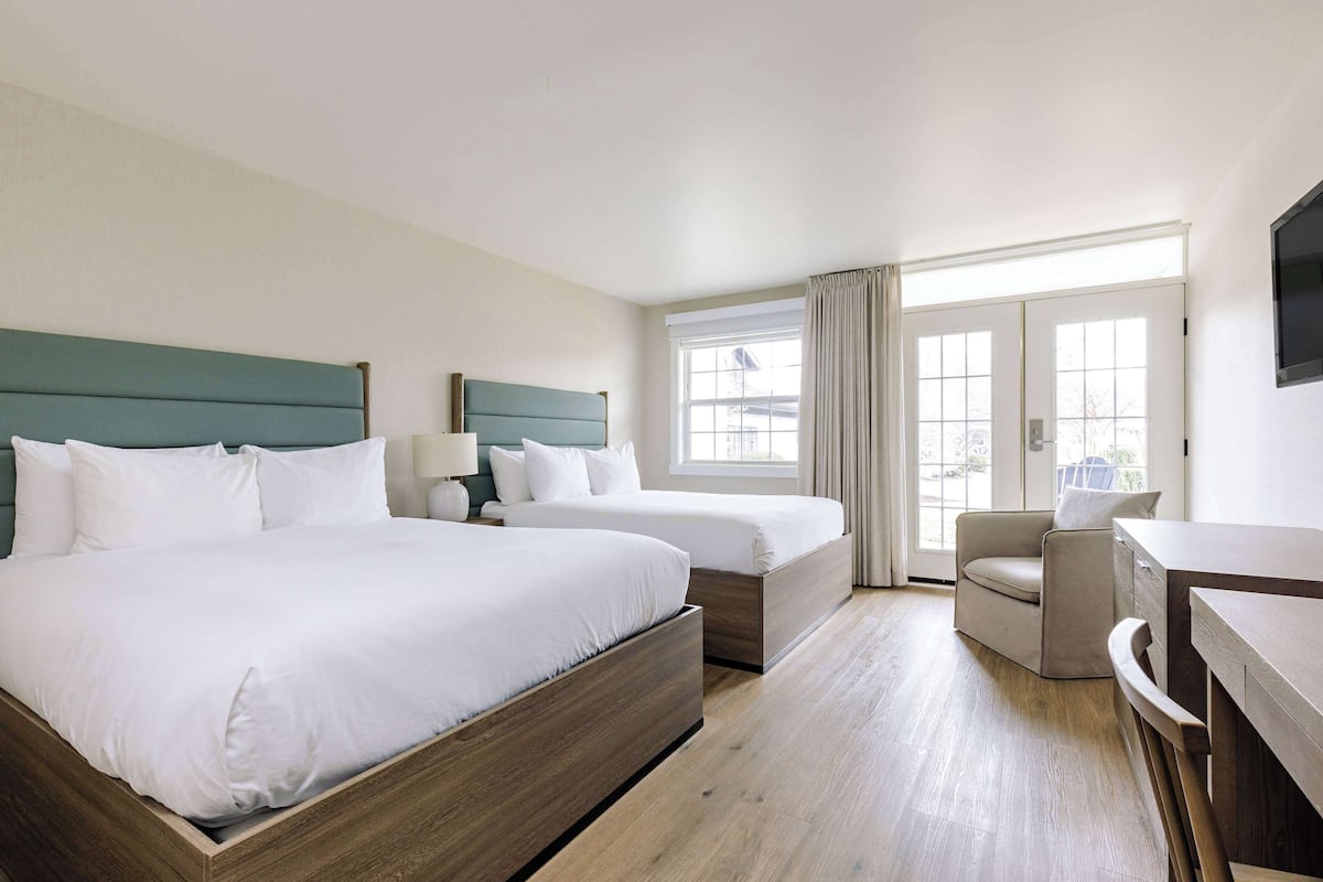 A hotel room with two beds, a desk, a chair, and a large window.