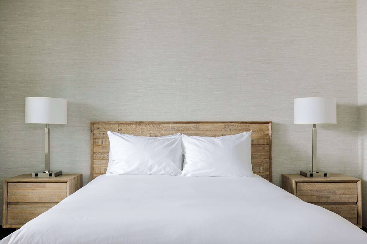 A neatly made bed with white linens and two bedside tables with lamps.