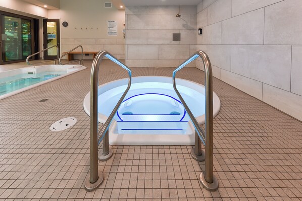 Un bain à remous doté d’une enceinte en verre et de garde-corps en métal, entouré d’un sol carrelé et d’une piscine.