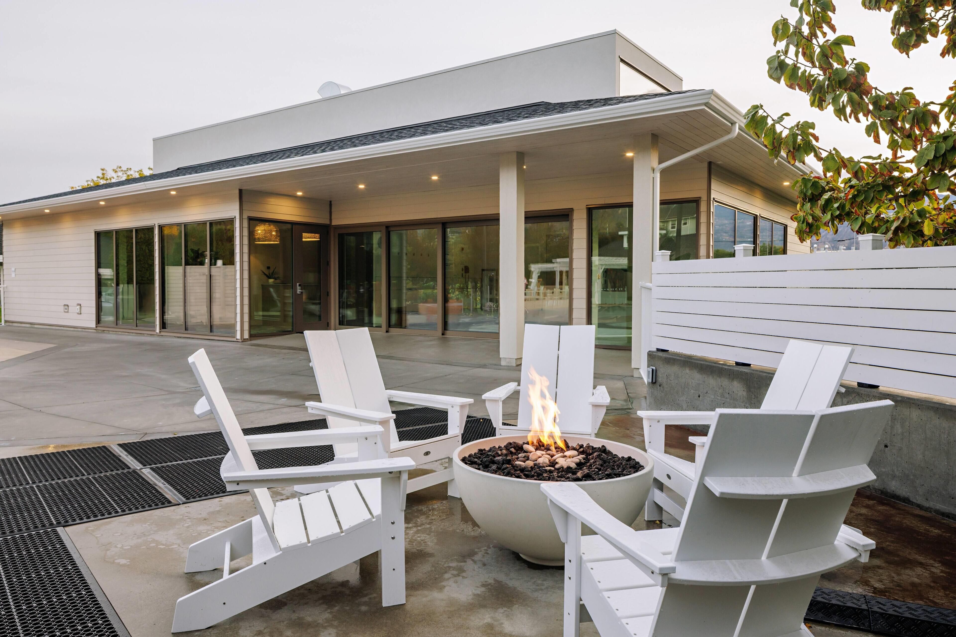 A modern outdoor seating area with white Adirondack chairs and a central fire pit.