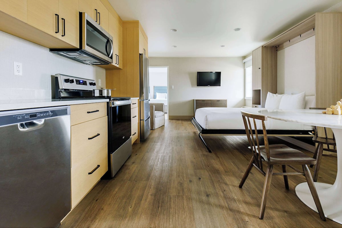 A modern kitchen with stainless steel appliances, wooden cabinets, and a dining area with a white table and chairs.