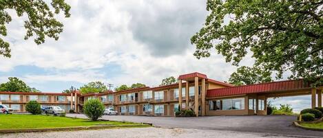 A motel with a red roof, multiple floors, and a parking lot.