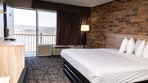 Une chambre d’hôtel avec un grand lit, un bureau, une chaise, une fenêtre avec des rideaux, un appareil de climatisation et un mur en briques.