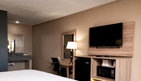 Habitación de hotel con cama, escritorio y silla, televisión de pantalla plana en la pared, microondas y refrigerador.