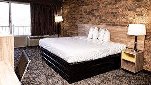 Une chambre d’hôtel avec un mur en briques, un lit avec une literie blanche, une table de chevet avec une lampe et un bureau avec une chaise.