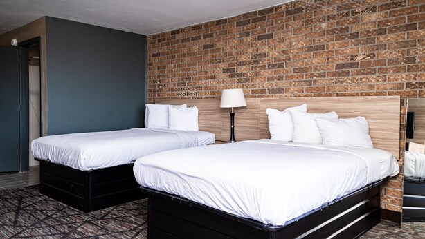 Une chambre d’hôtel avec deux lits simples, un mur en briques, une tête de lit en bois et une moquette à motifs.