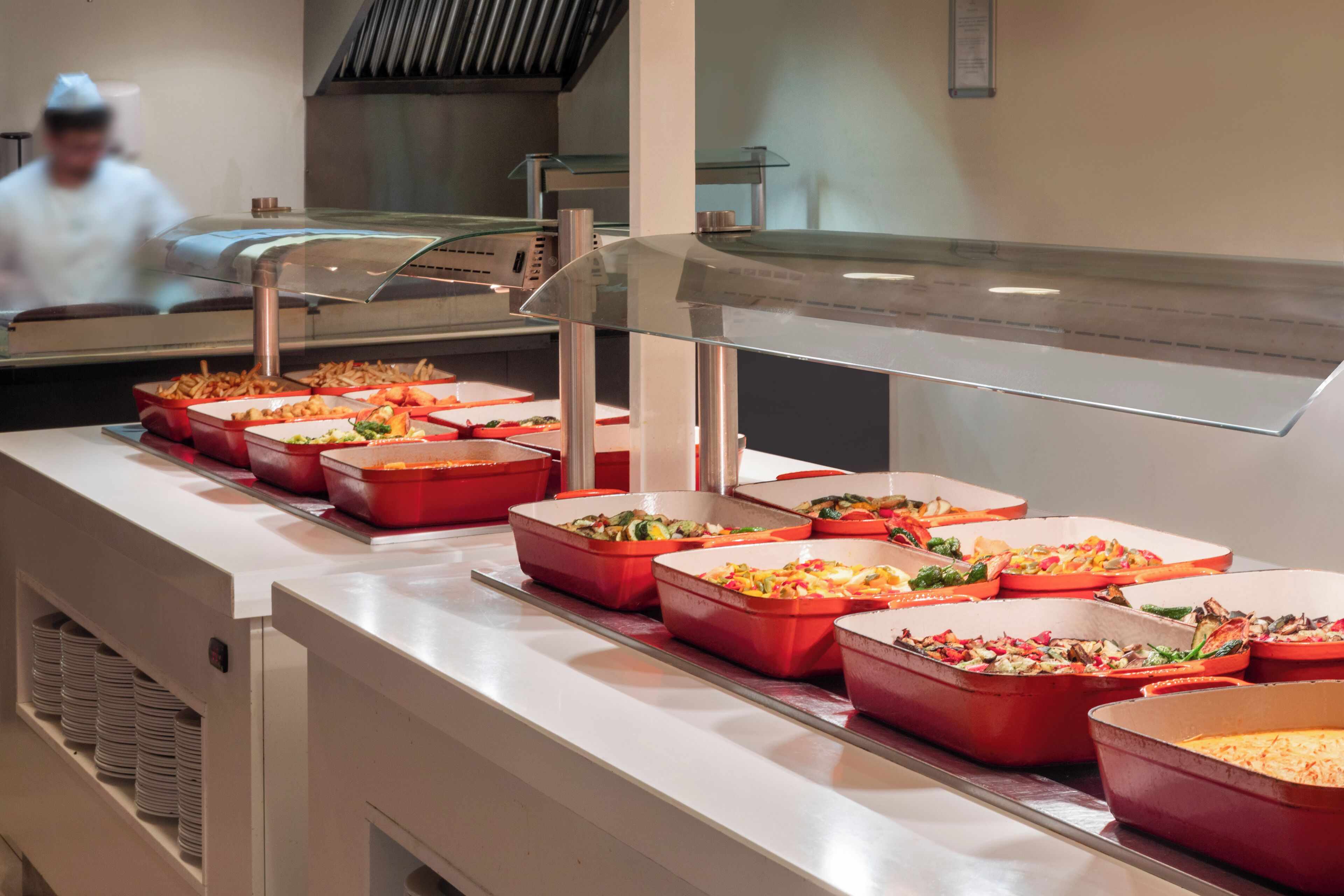 A buffet line with various food dishes in red trays.