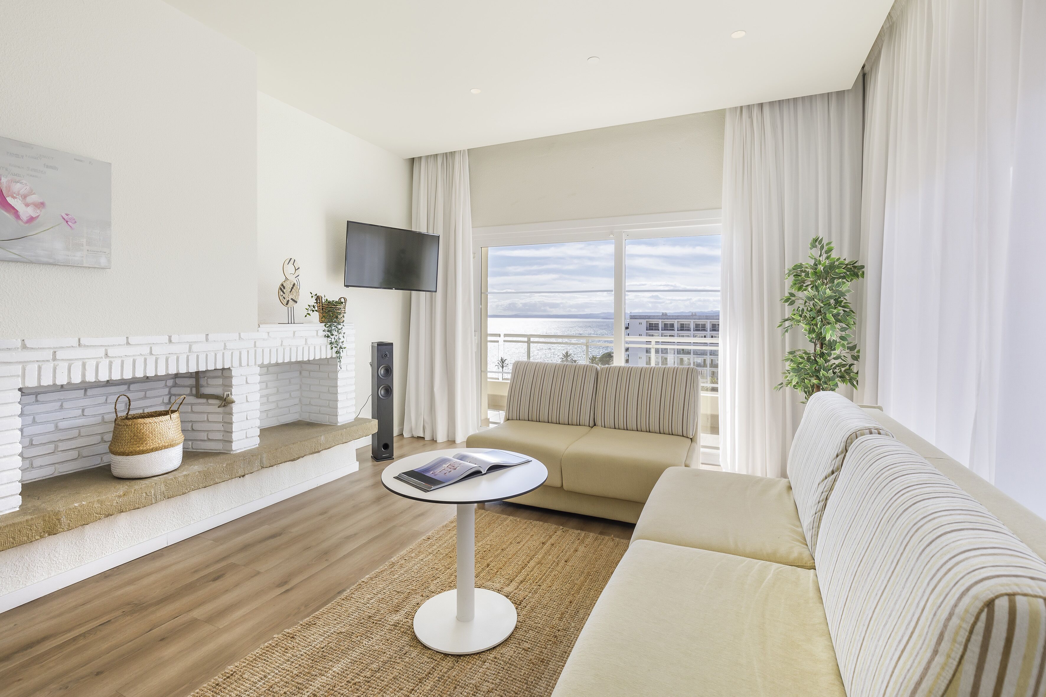 A modern living room with a white brick fireplace, a beige sofa, a round coffee table, and a large window with a view of the city.