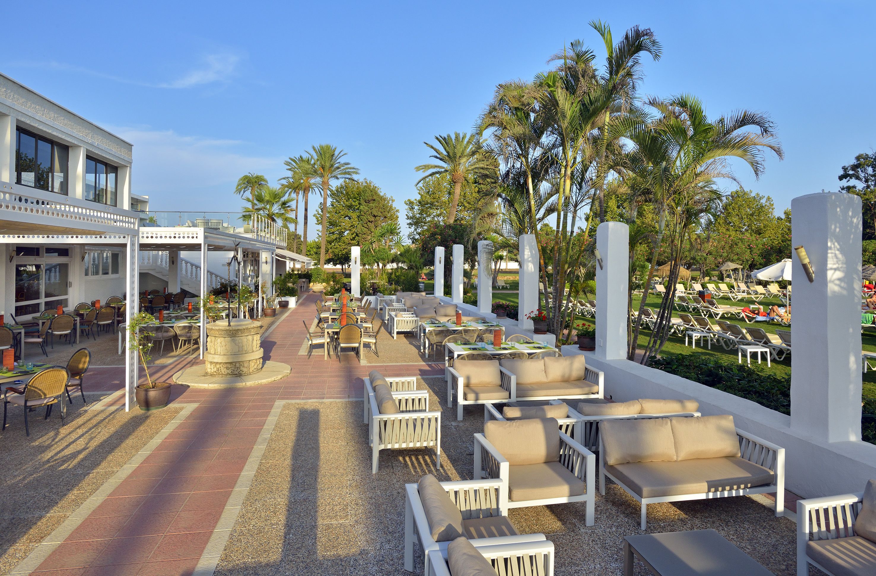 An outdoor seating area with white furniture, palm trees, and a building with large windows.