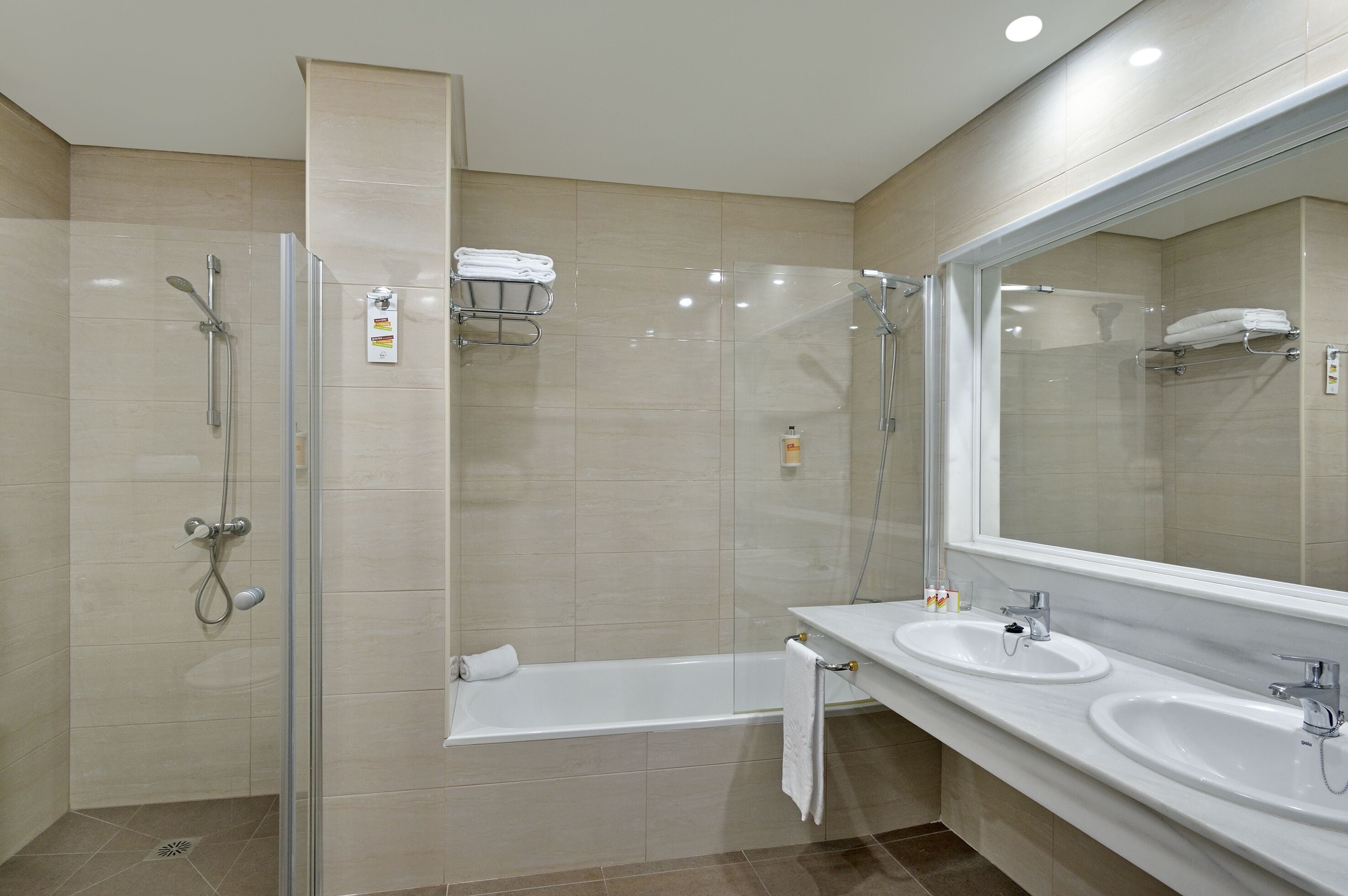 A modern bathroom with a glass-enclosed shower, a bathtub, and two sinks.