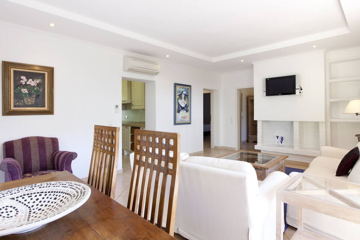 Una sala moderna con una mesa de comedor, sillas, un sofá y un televisor montado en la pared.