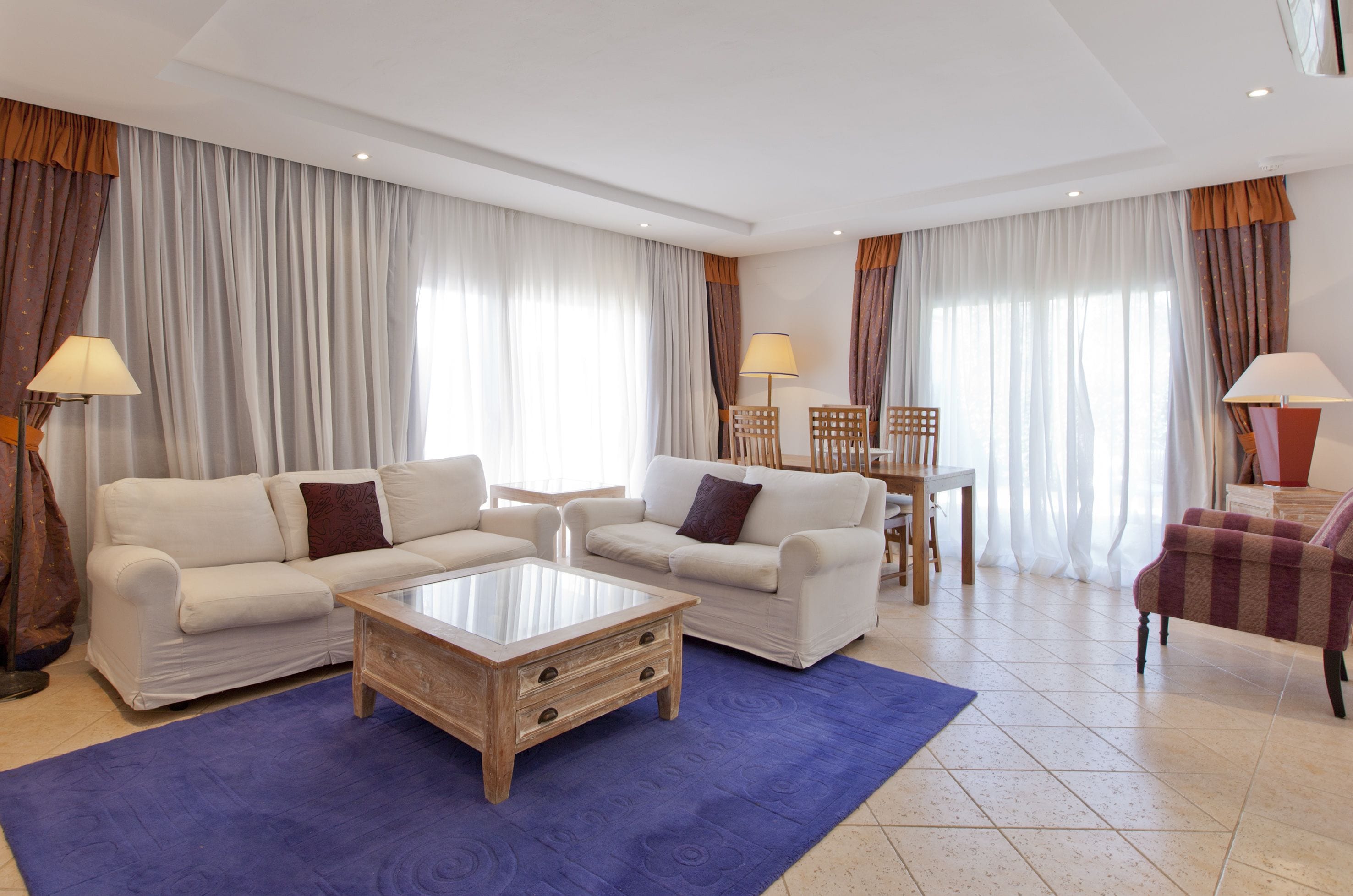 A spacious living room with two white sofas, a wooden coffee table, and a dining area with a table and chairs.