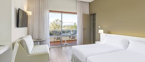A hotel room with a bed, a sofa, a TV mounted on the wall, and a balcony with a table and chairs.