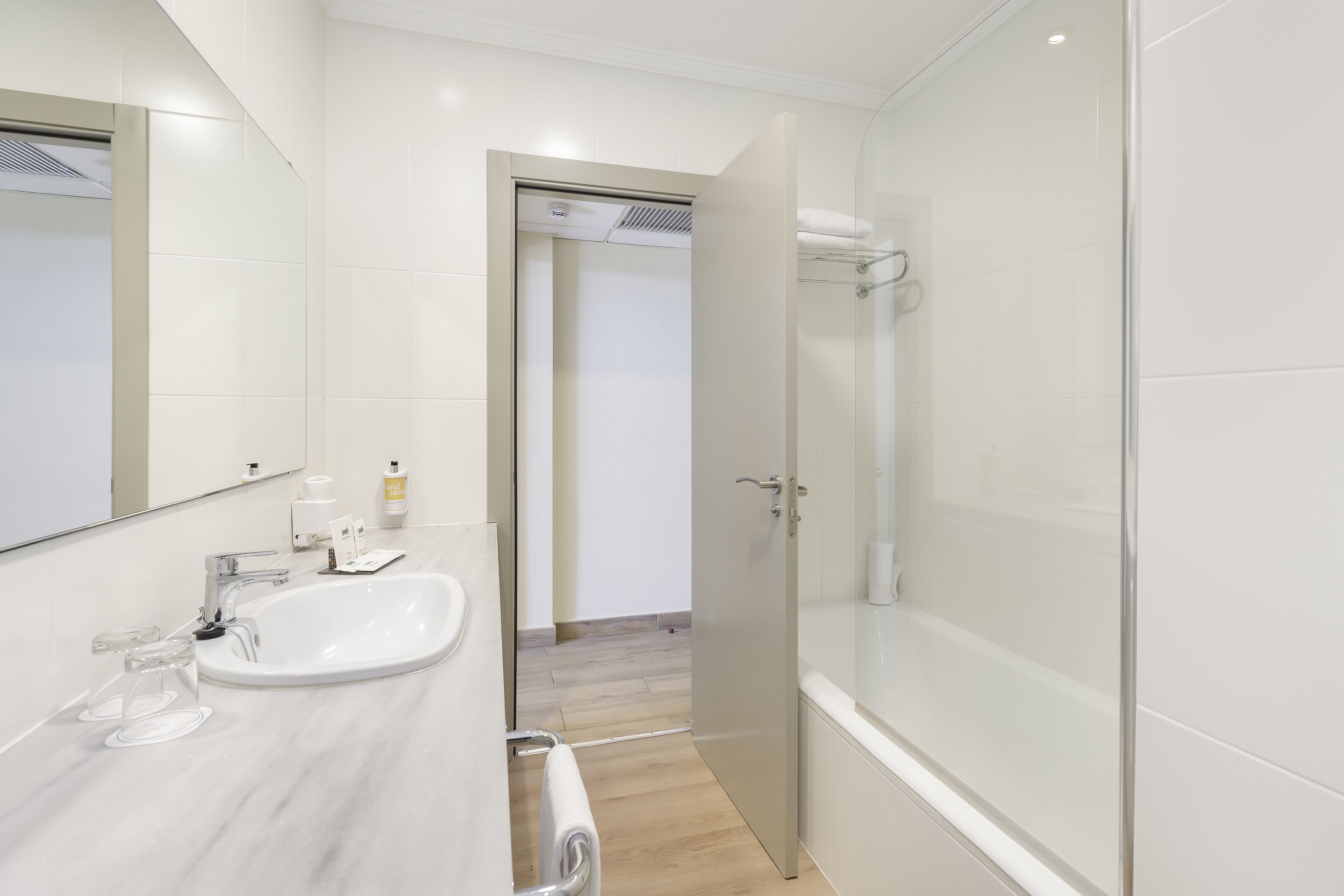 Un baño moderno con un espejo grande, un lavamanos y una ducha con mampara de vidrio.