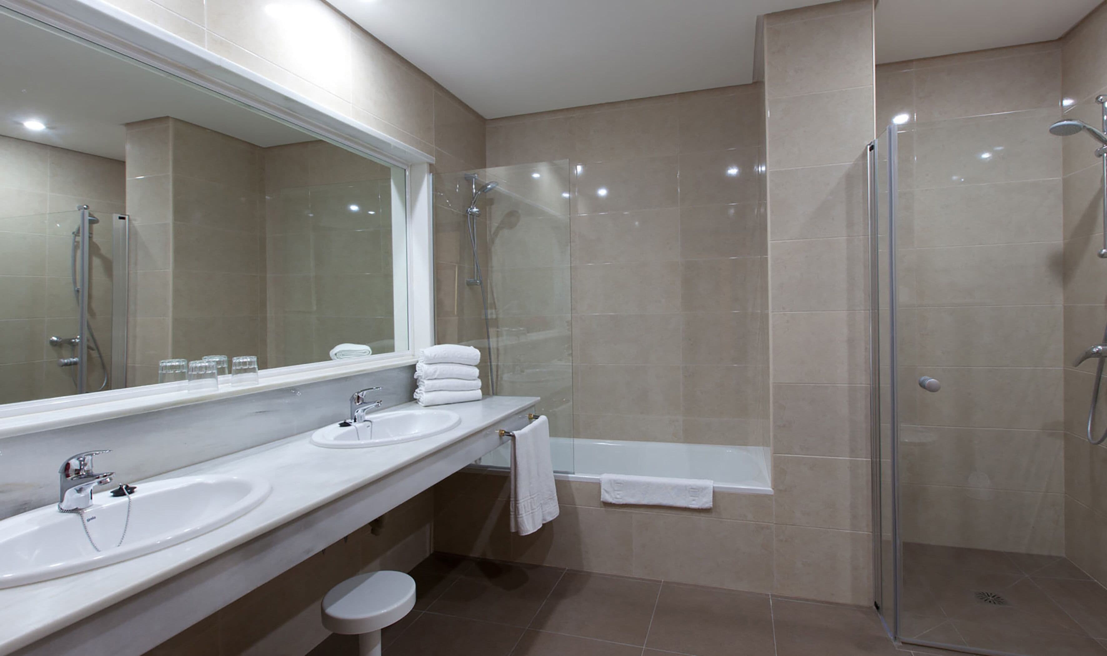 A modern bathroom with two sinks, a large mirror, a glass-enclosed shower, and a bathtub.