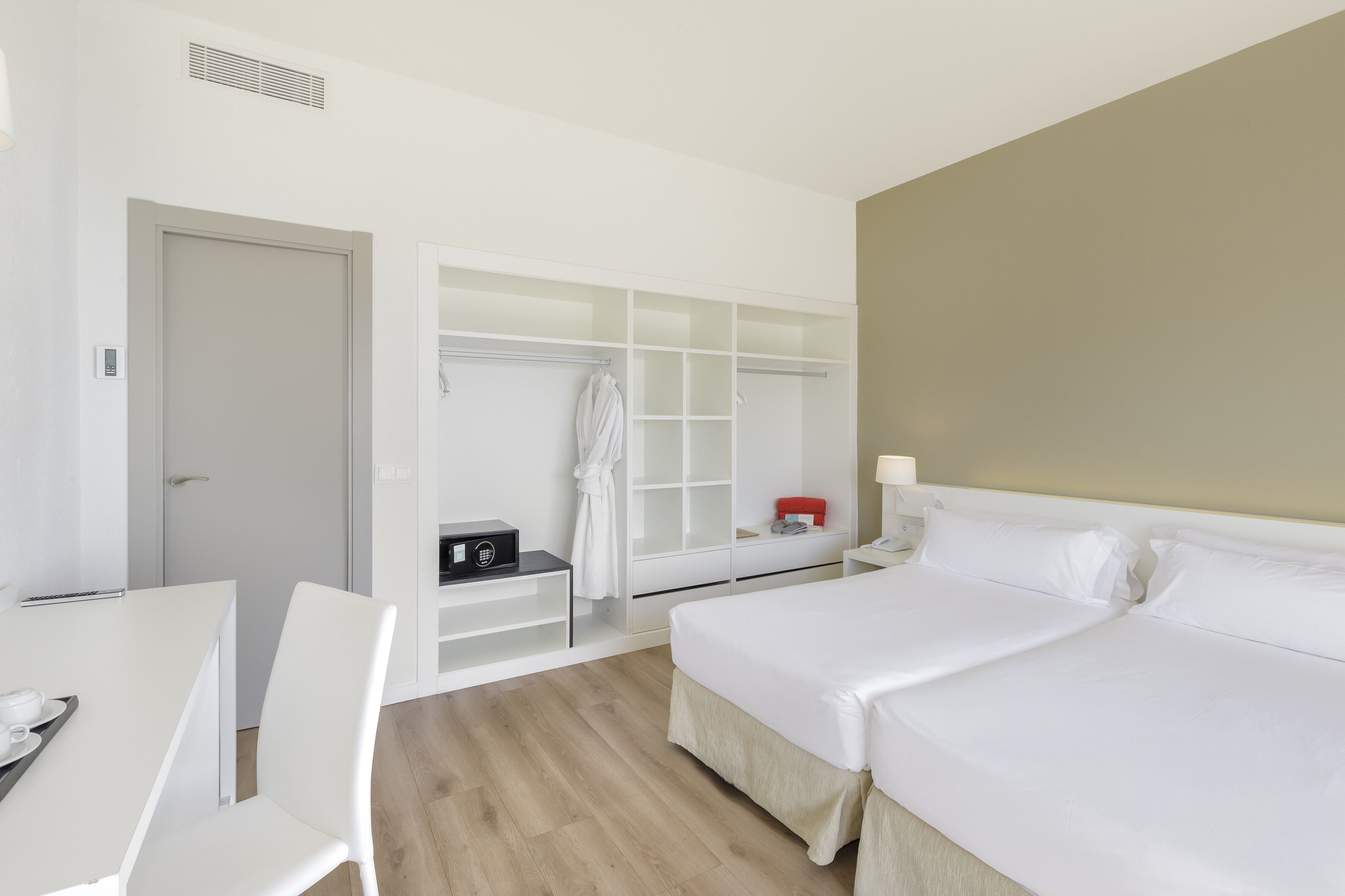 Habitación de hotel con cama, escritorio, silla, armario y mesita de noche.