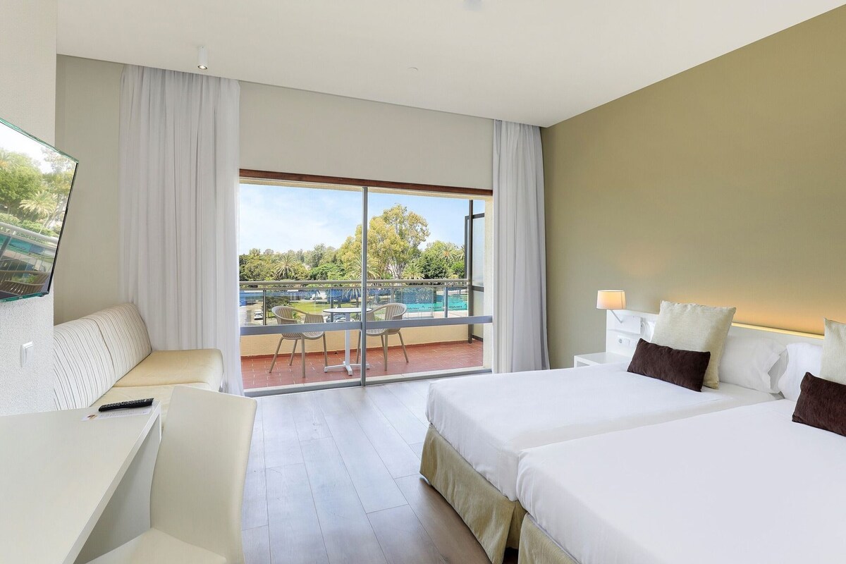 A hotel room with a balcony, a bed, a desk, and a chair.