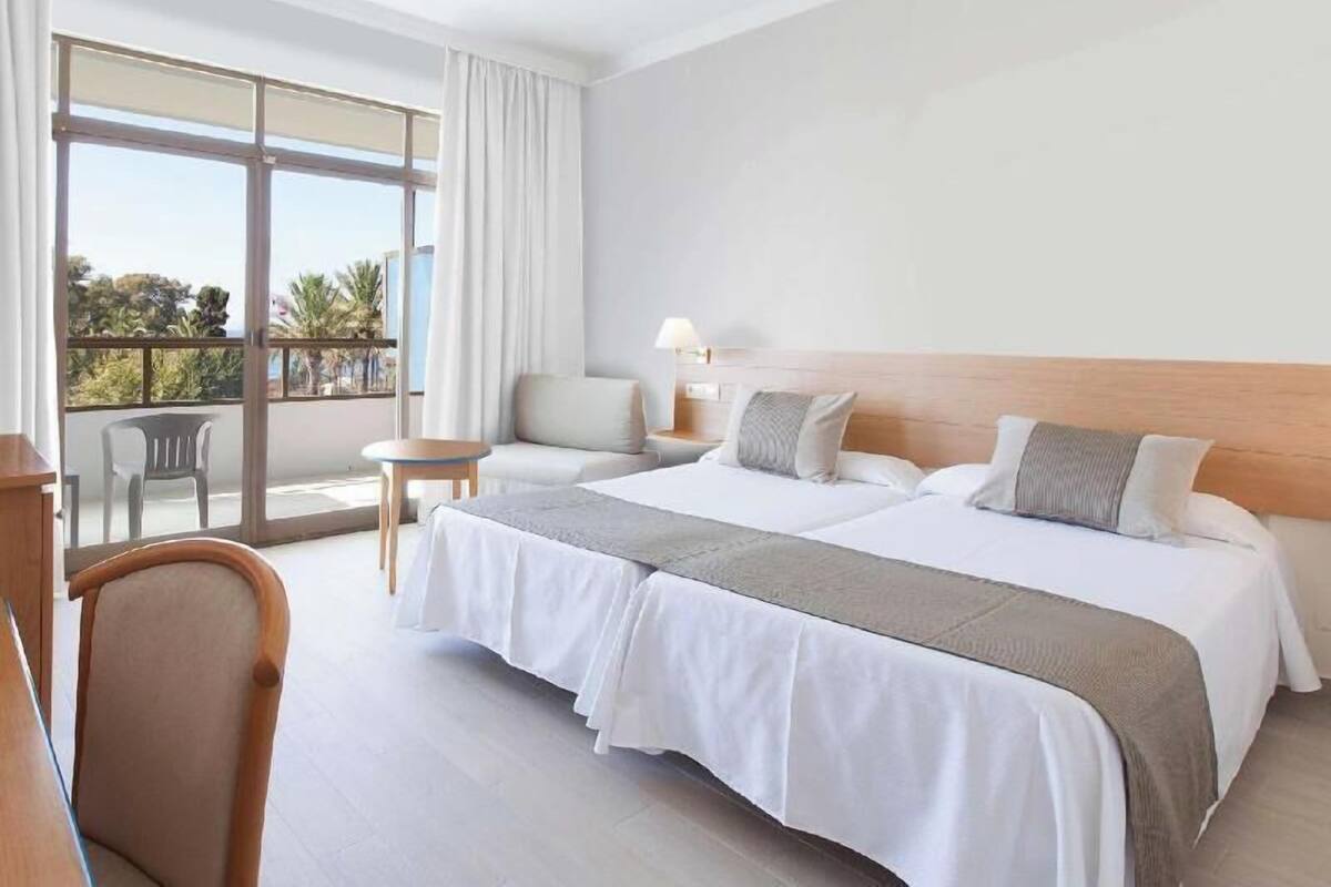 Habitación de hotel con una cama grande, un escritorio, una silla, una mesita y un balcón con vistas.