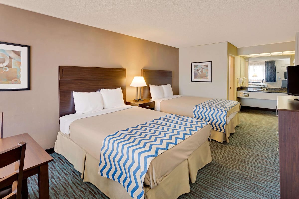 A hotel room with two beds, a desk, a chair, a lamp, a television, and a mirror.