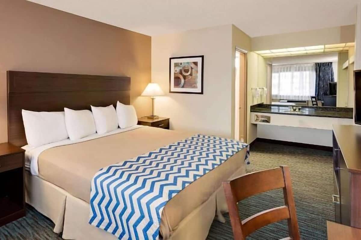 A hotel room with a bed, two bedside lamps, a desk, a chair, a television, a framed picture on the wall, and a bathroom visible through an open door.