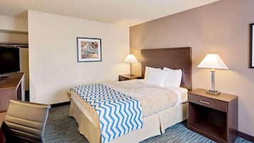 A hotel room with a bed, two bedside tables with lamps, a desk with a chair, and a television.