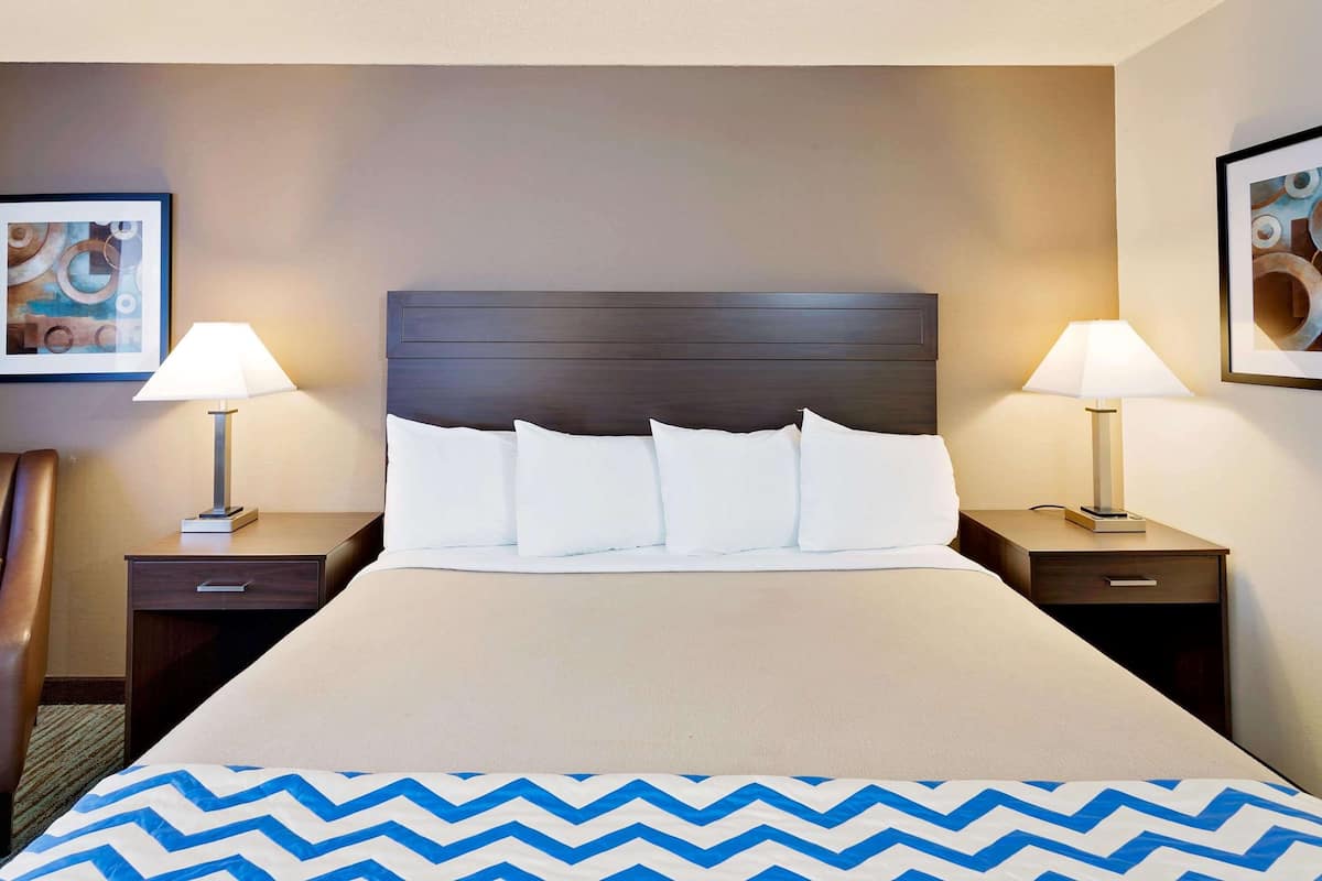 A hotel room with a large bed, two bedside tables, a chair, and artwork on the walls.